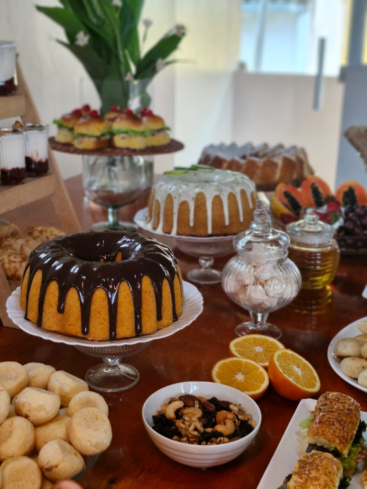 Mesa de coffee break com bolos, pães de queijo, frutas e sanduíches